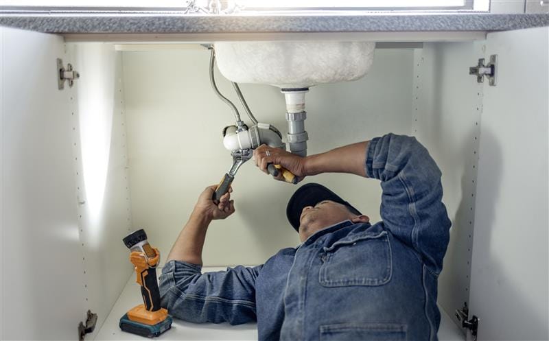 Plumber repairing pipes beneath a bathroom sink in Westminster