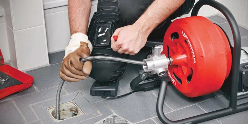 Plumber using a drain-cleaning machine in Westminster