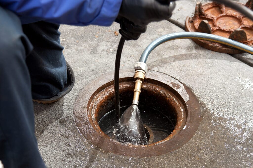 Plumber hydro jetting a sewer line through a manhole in Westminster