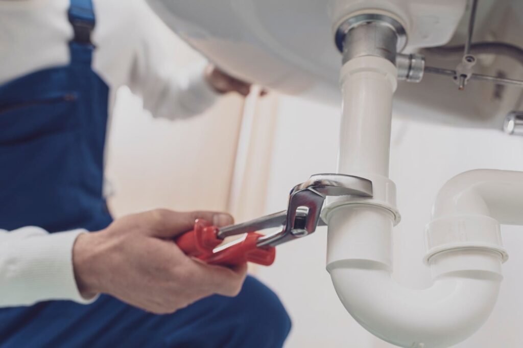 Plumber repairing a white drain pipe beneath a sink in Westminster