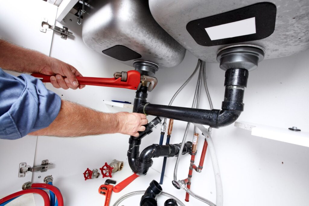 Plumber repairing drain pipes beneath a kitchen sink in Westminster