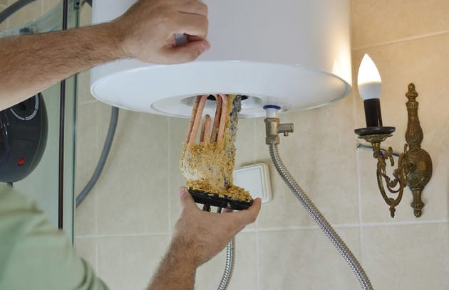 Technician removing mineral buildup from a water heater in Westminster